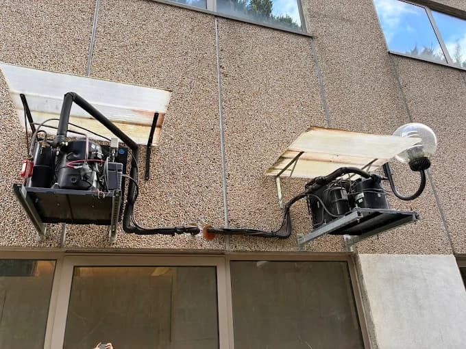 Deux groupes de condensation noirs fixés en façade d'immeuble lors d'un entretien de climatisation